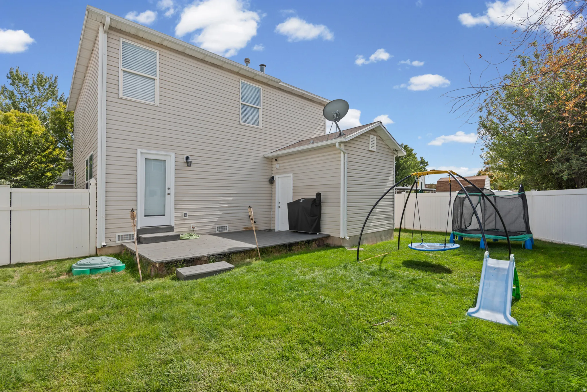 Expansive lawn area with a multi-level patio, vinyl siding exterior, and privacy fencing