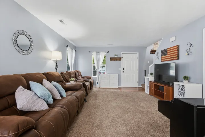 Spacious living area featuring light blue wall paint, a white entry door, and recessed lighting