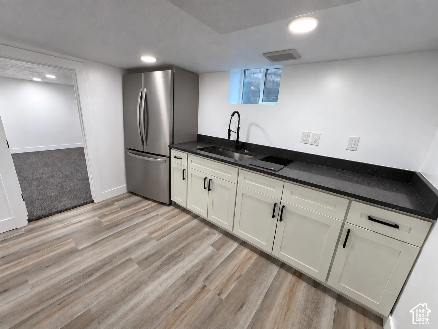 Kitchenette featuring wood-finish flooring, white cabinetry with black hardware, dark countertops, and a stainless steel refrigerator