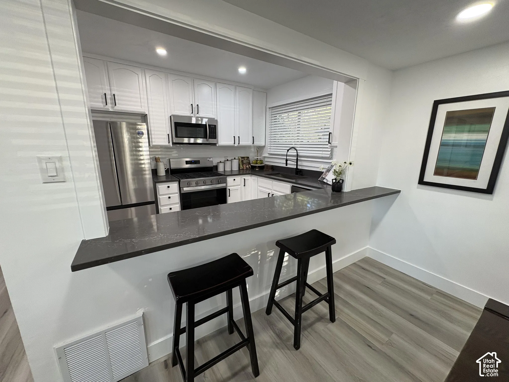 Open-concept kitchen featuring white cabinetry with dark hardware, stainless steel appliances, dark countertops, and a pass-through bar