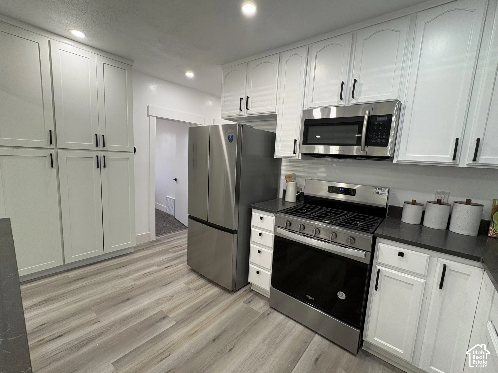 Kitchen featuring white cabinetry with black hardware, stainless steel appliances, dark countertops, and wood-finish flooring