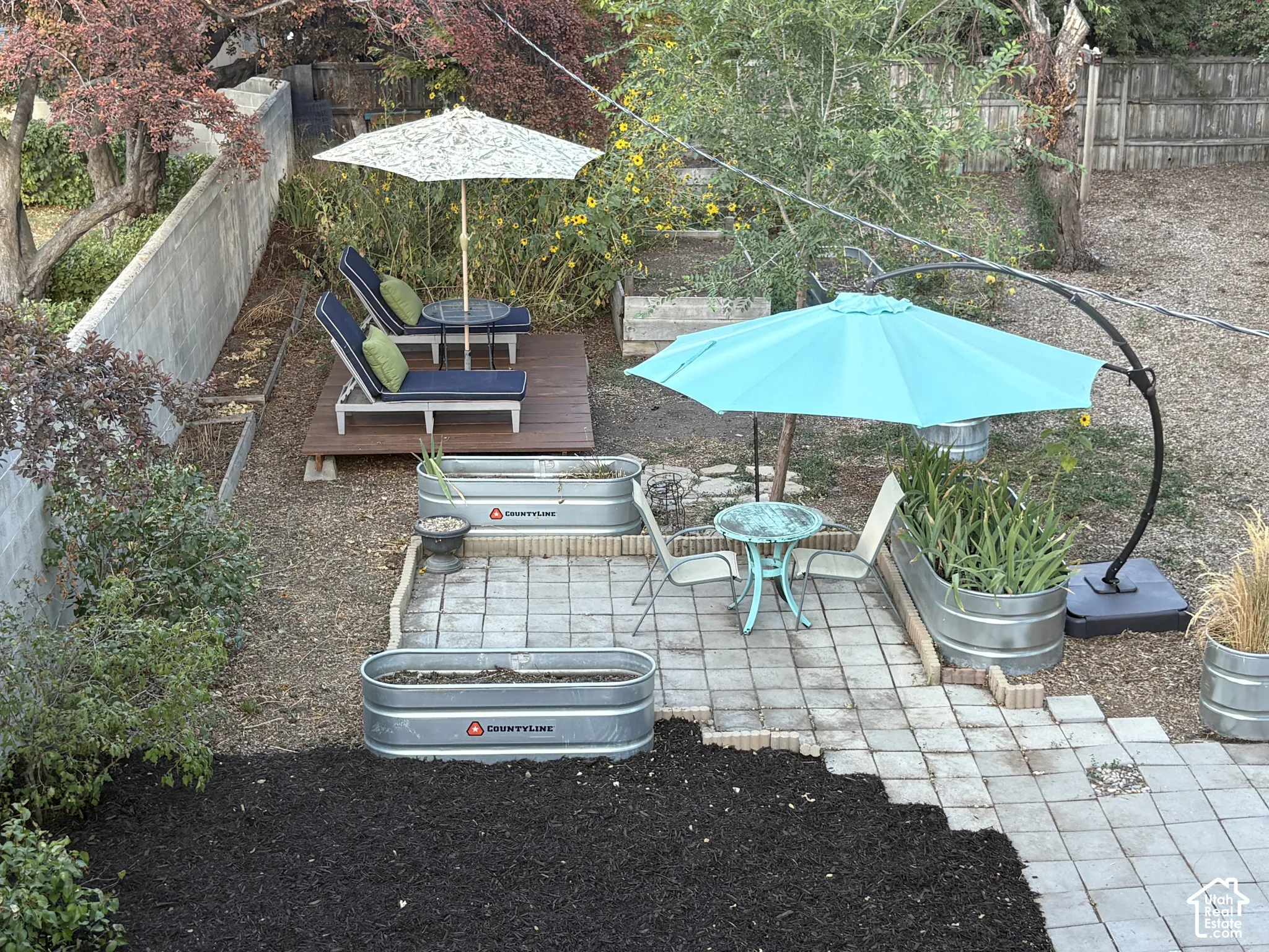 Tiered backyard featuring a paver patio area, elevated wood deck, and multiple galvanized metal planters