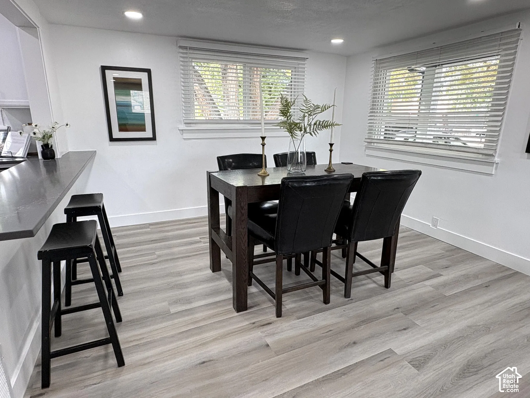 Open-concept dining area featuring wood-finish flooring, recessed lighting, and a breakfast bar with a solid surface countertop