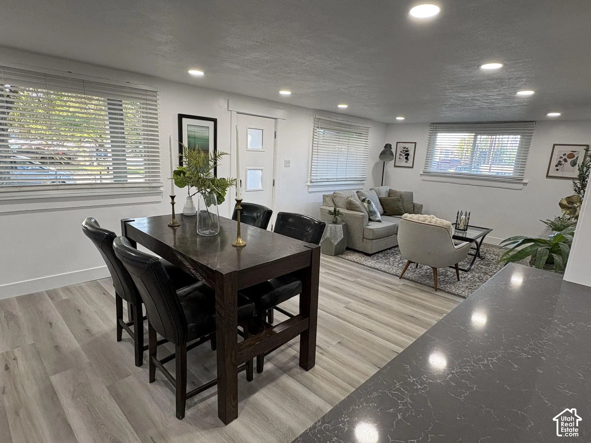 Recessed lighting, wood-finish flooring, white walls, multiple windows, and a dark stone-finish countertop