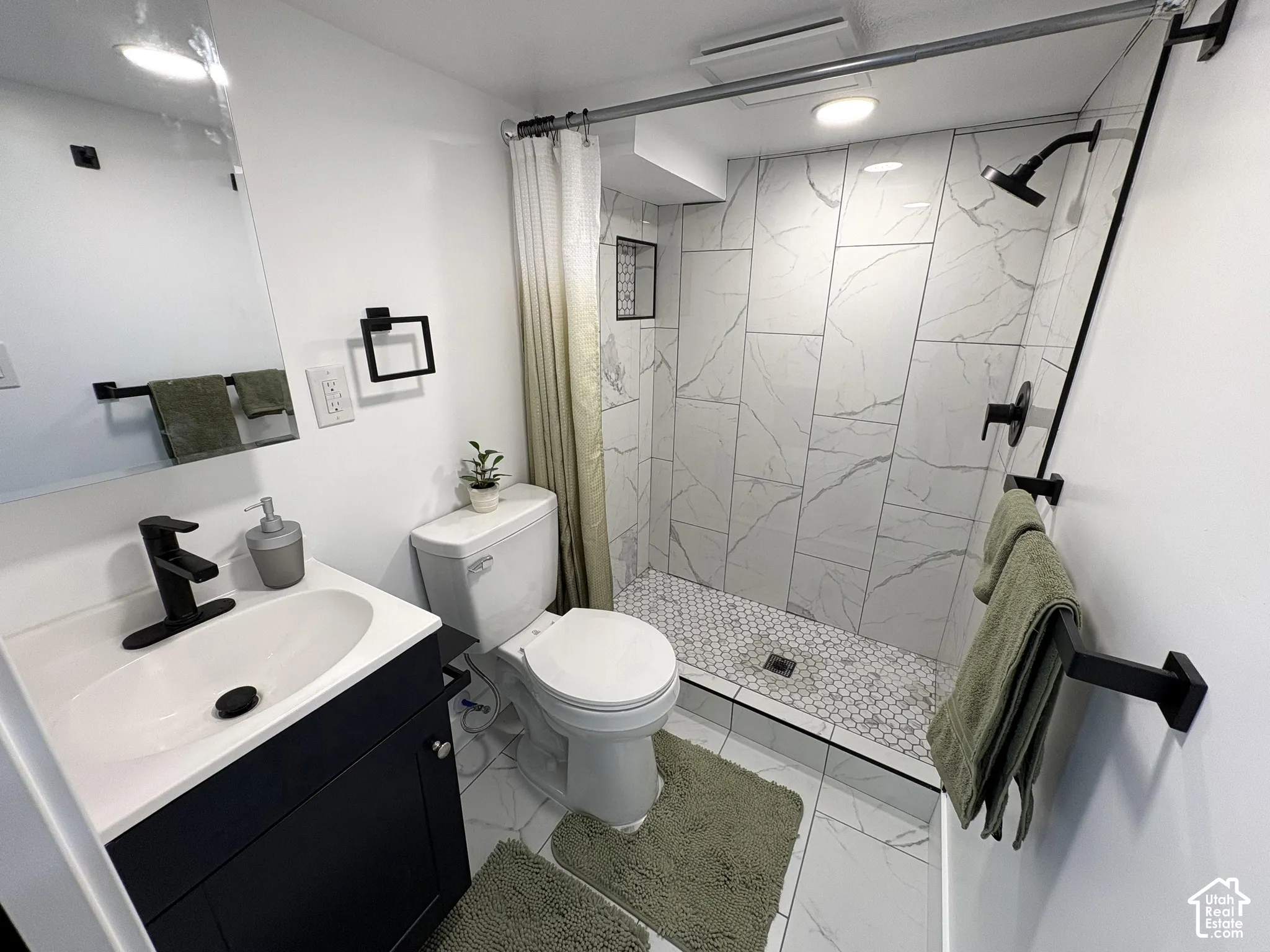 Bathroom featuring large format wall tile, a walk-in shower with mosaic tile flooring, a dark wood-finish vanity with a white countertop, and matte black fixtures