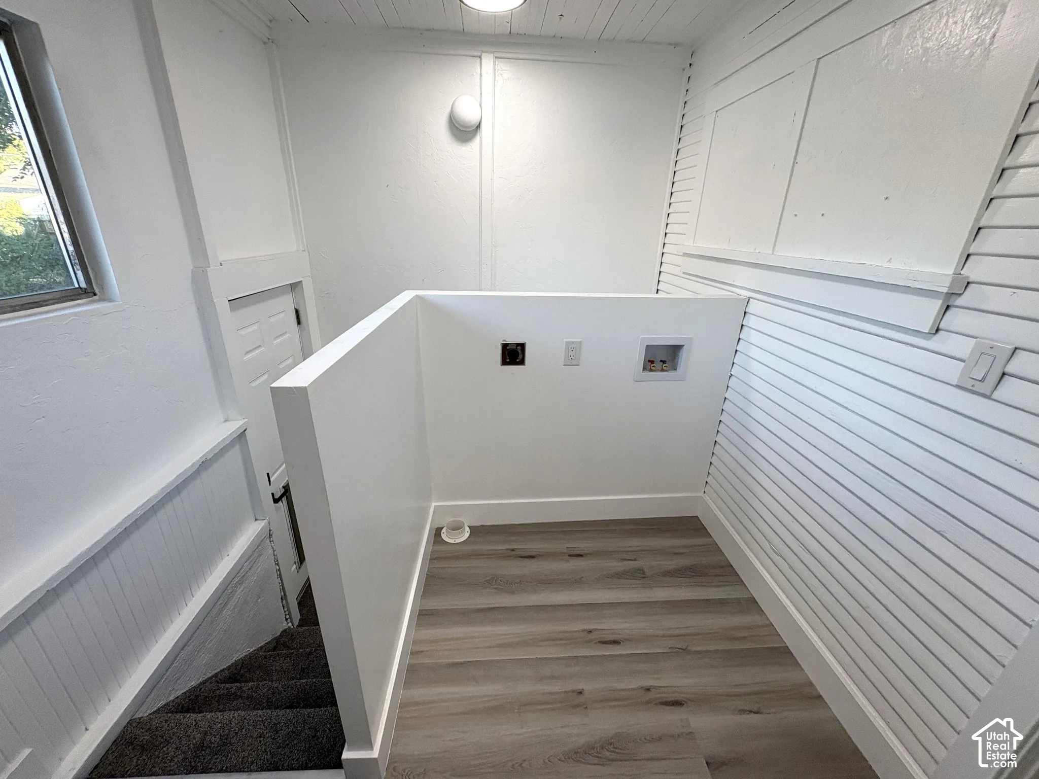 Dedicated laundry area featuring wood-finish flooring, white shiplap walls, and a convenient window