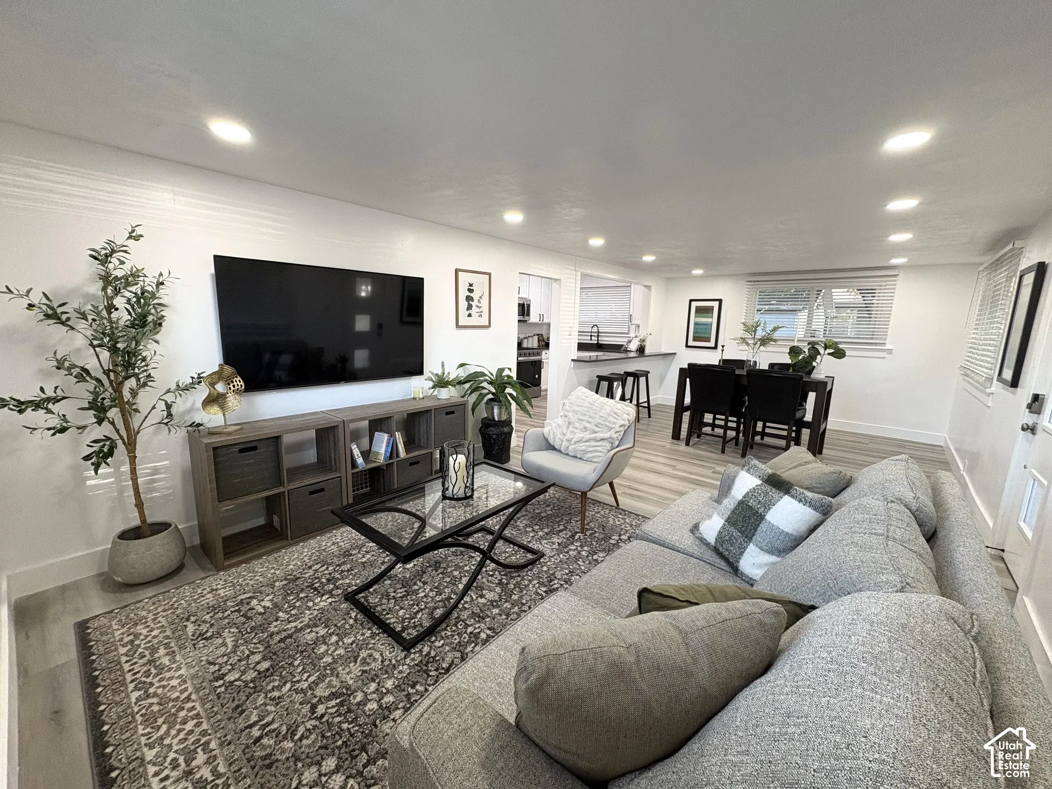 Recessed lighting illuminating the open-concept living space, featuring wood-finish flooring and a kitchen with dark countertops
