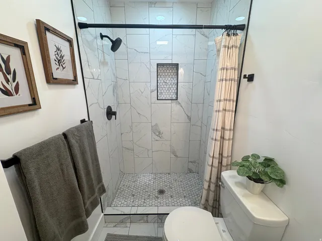 Walk-in shower with full height tile surround, hexagonal tile shower floor, and a built-in shower niche