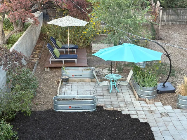 Tiered backyard featuring a paver patio area, elevated wood deck, and multiple galvanized metal planters