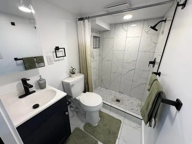 Bathroom featuring large format wall tile, a walk-in shower with mosaic tile flooring, a dark wood-finish vanity with a white countertop, and matte black fixtures