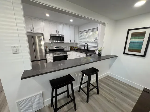 Open-concept kitchen featuring white cabinetry with dark hardware, stainless steel appliances, dark countertops, and a pass-through bar