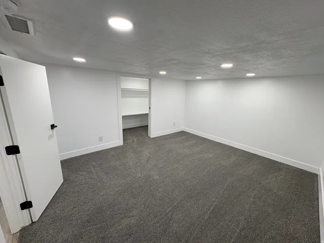 Recessed ceiling lighting, white walls, gray carpeting, white trim, and a built-in closet with shelving
