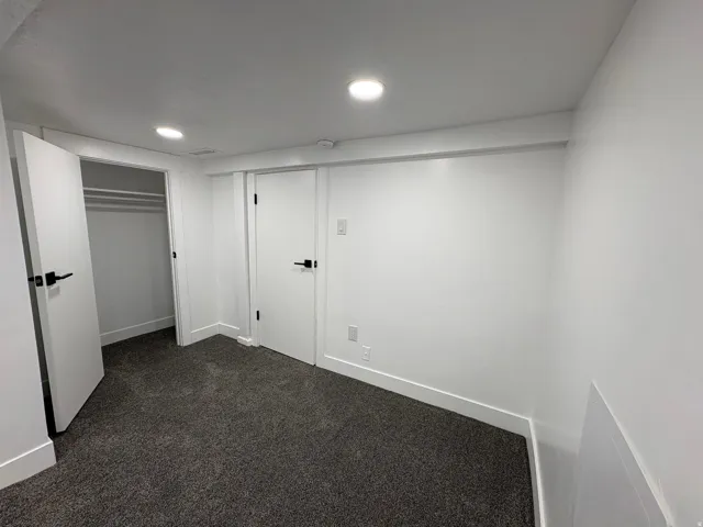 Recessed lighting, white walls, dark gray carpeting, white interior doors, and matte black hardware