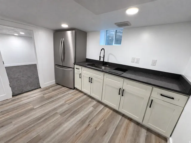 Kitchenette featuring wood-finish flooring, white cabinetry with black hardware, dark countertops, and a stainless steel refrigerator