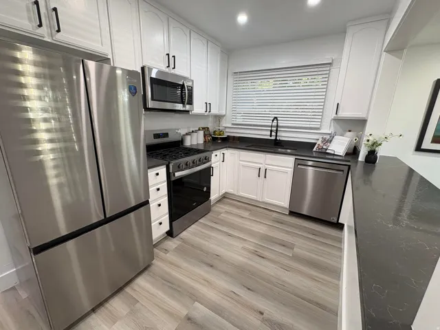 Kitchen featuring stainless steel appliances, dark countertops, white cabinetry with black hardware, and wood-finish flooring