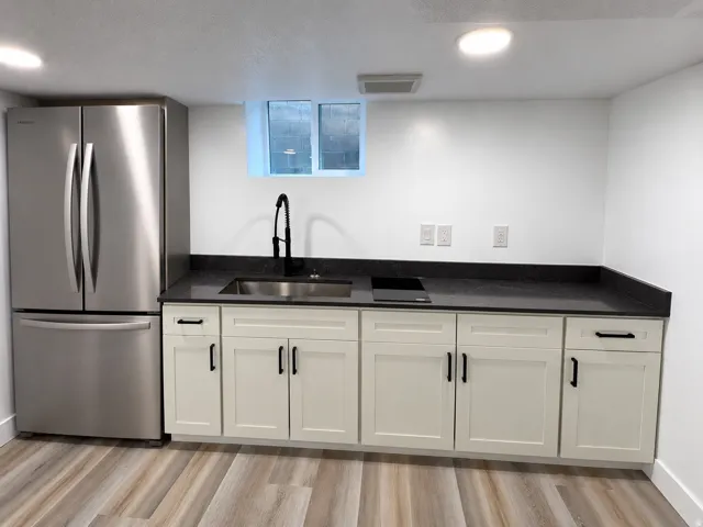 Stainless steel French door refrigerator, dark countertop, single-basin sink with matte black faucet, light-colored cabinetry with matte black hardware, and wood-finish flooring