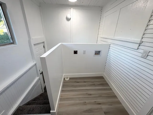 Dedicated laundry area featuring wood-finish flooring, white shiplap walls, and a convenient window