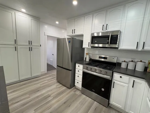 Kitchen featuring white cabinetry with black hardware, stainless steel appliances, dark countertops, and wood-finish flooring