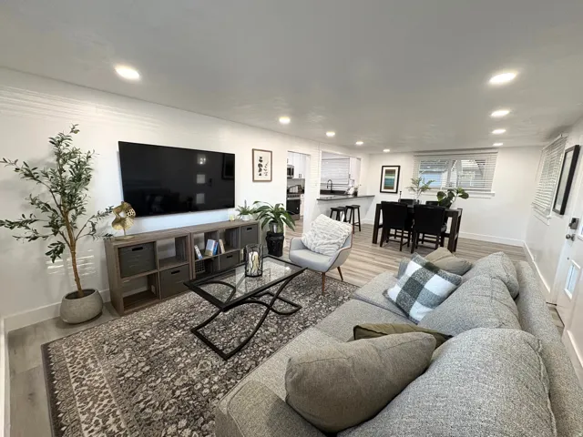 Recessed lighting illuminating the open-concept living space, featuring wood-finish flooring and a kitchen with dark countertops