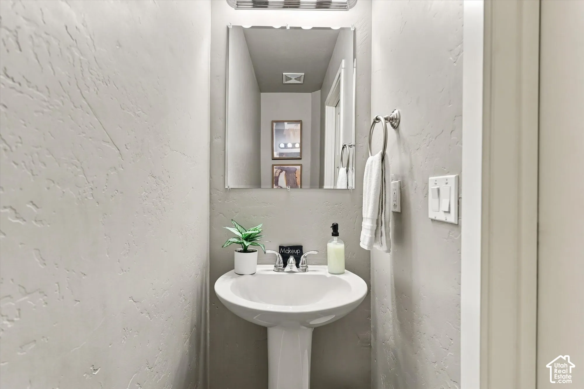 Pedestal sink with chrome faucet, framed mirror, and textured wall finish