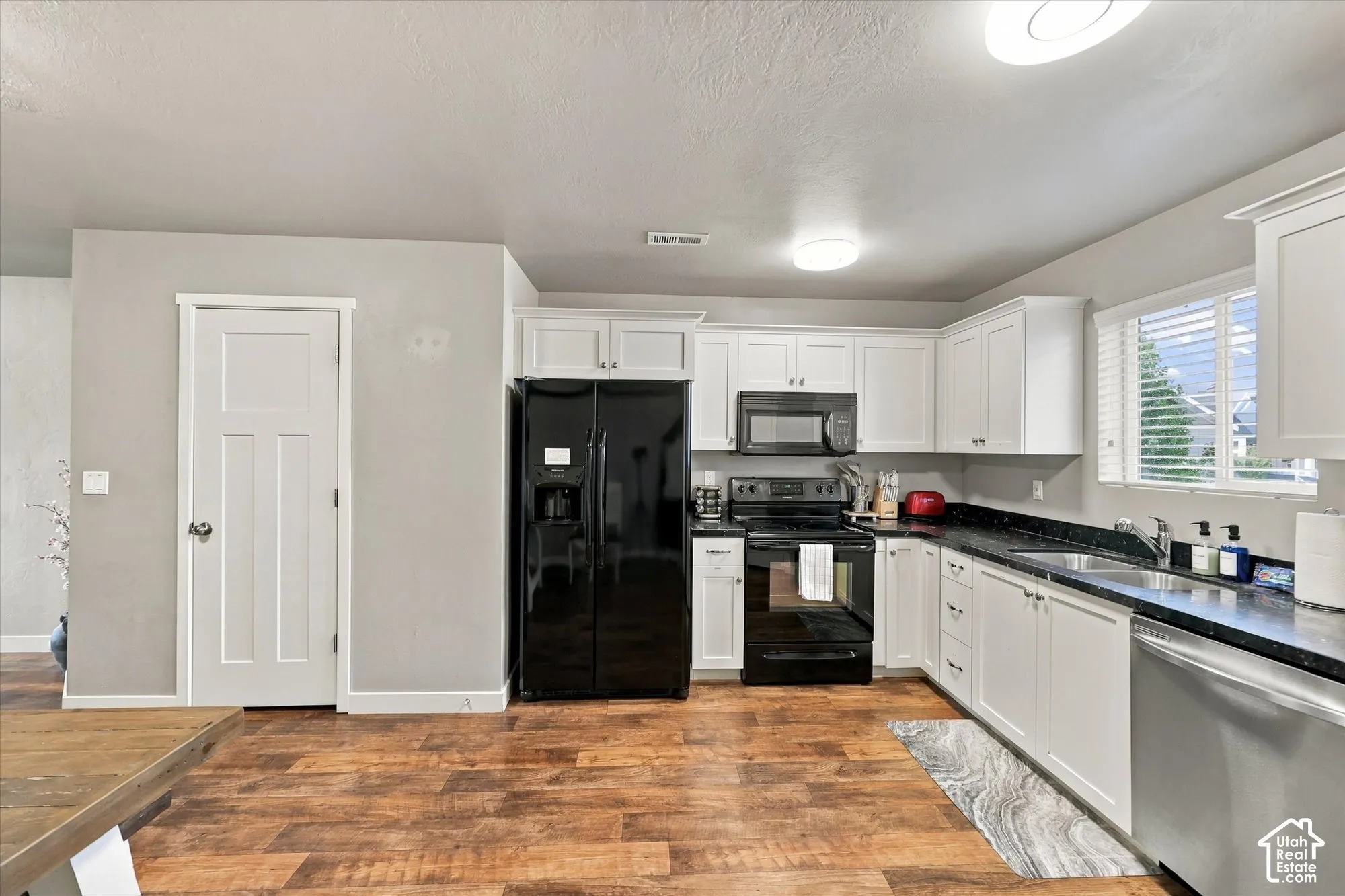 Kitchen featuring wood-finish flooring, white cabinetry, black appliances, dark countertops, and a stainless steel dishwasher
