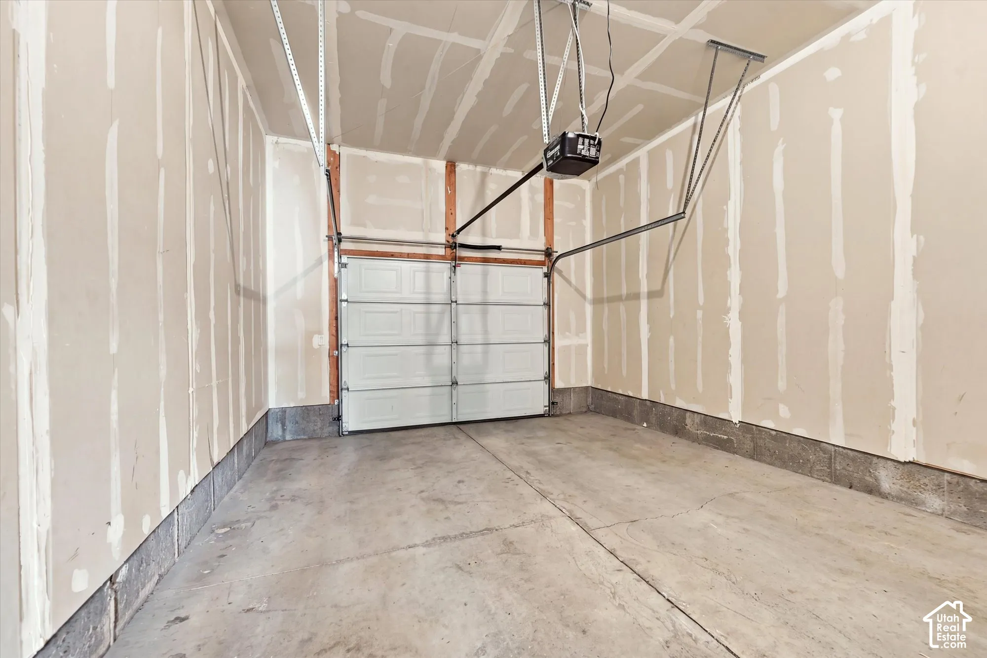 Attached garage featuring a concrete floor, automatic garage door opener, and unfinished drywall walls