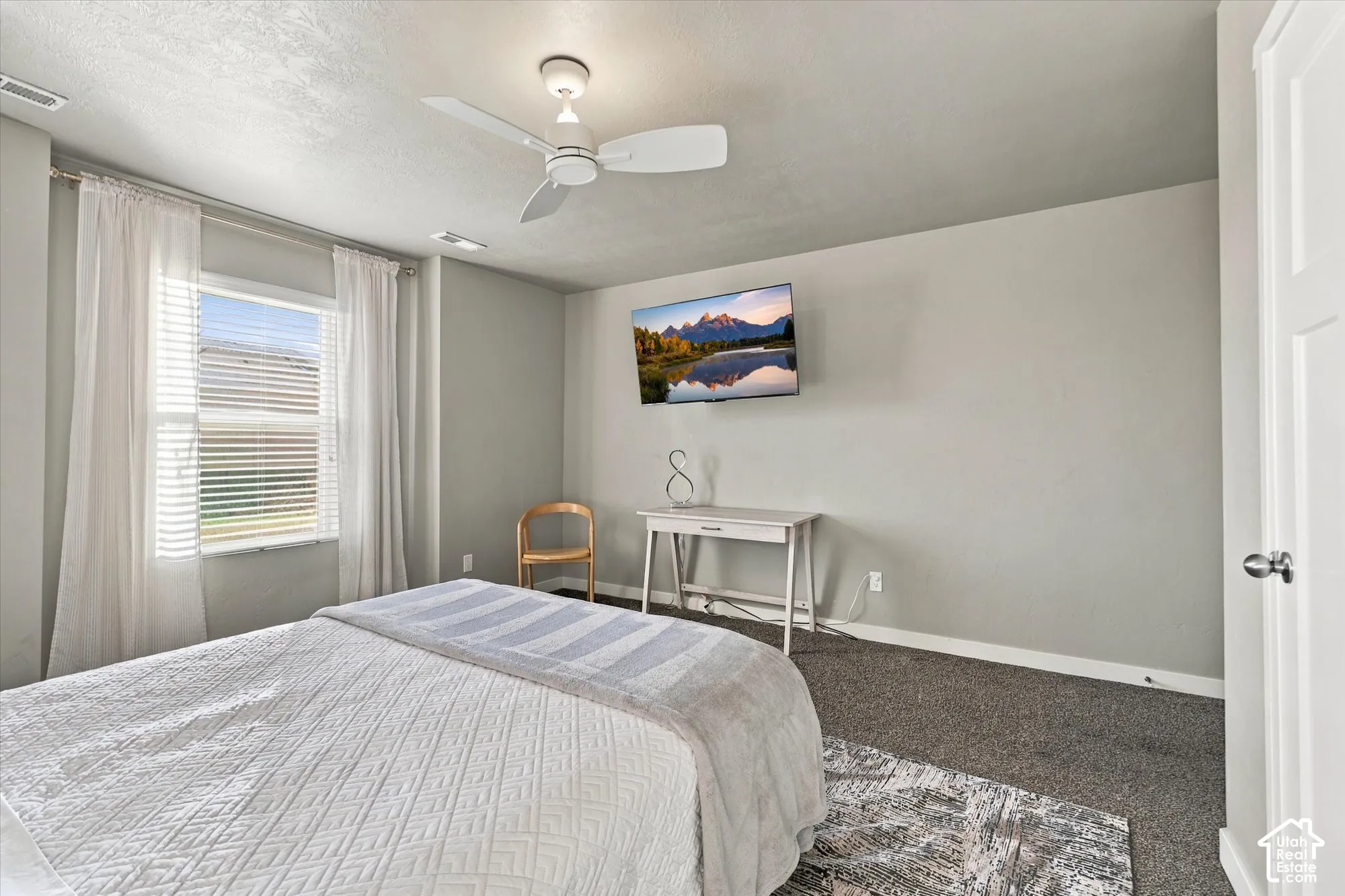 Carpeted flooring with a contrasting area rug, light-colored walls, a ceiling fan, and a single window with blinds
