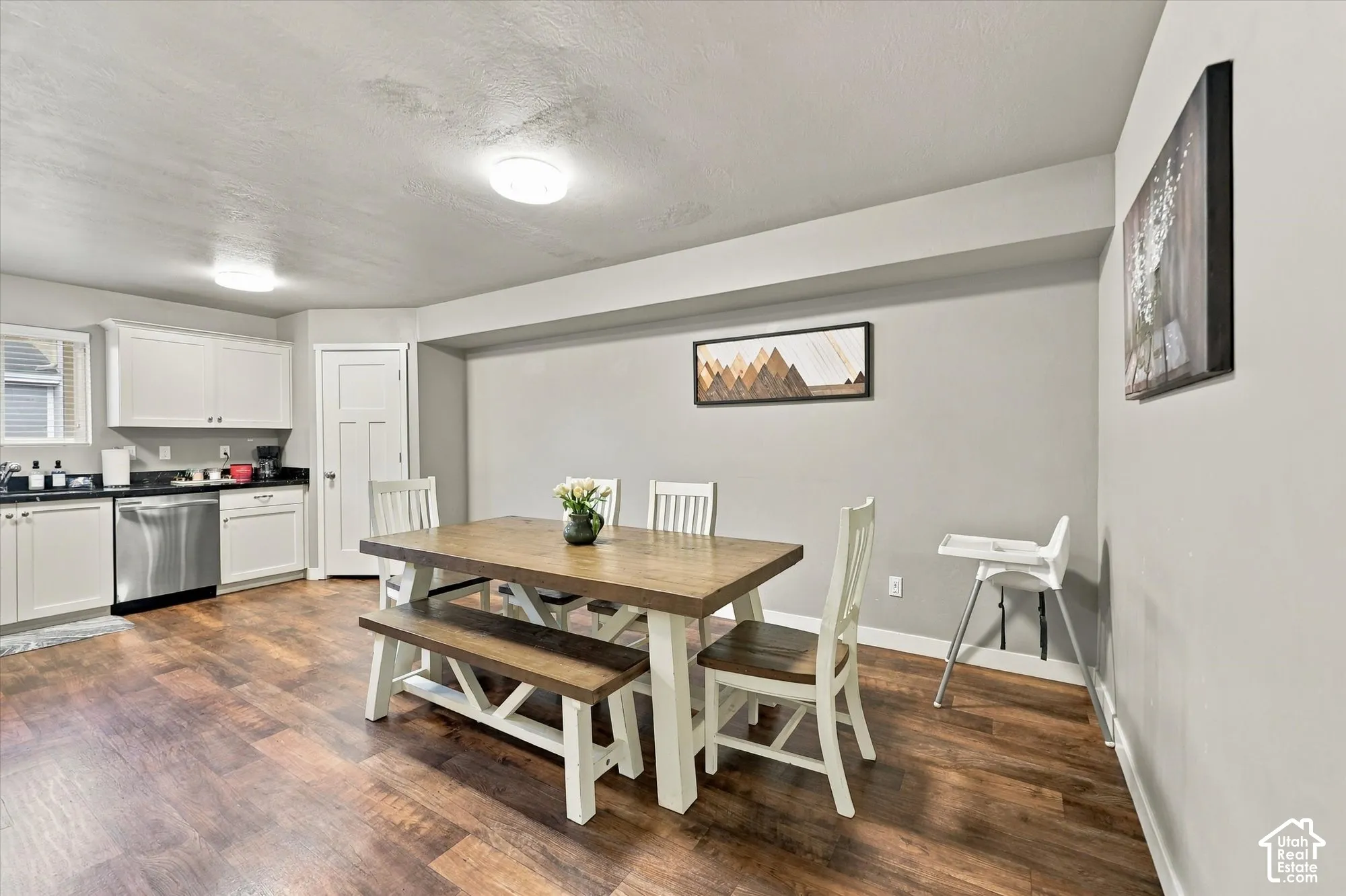 Wood-finish flooring throughout, white cabinetry with dark countertops, stainless steel dishwasher, and recessed lighting