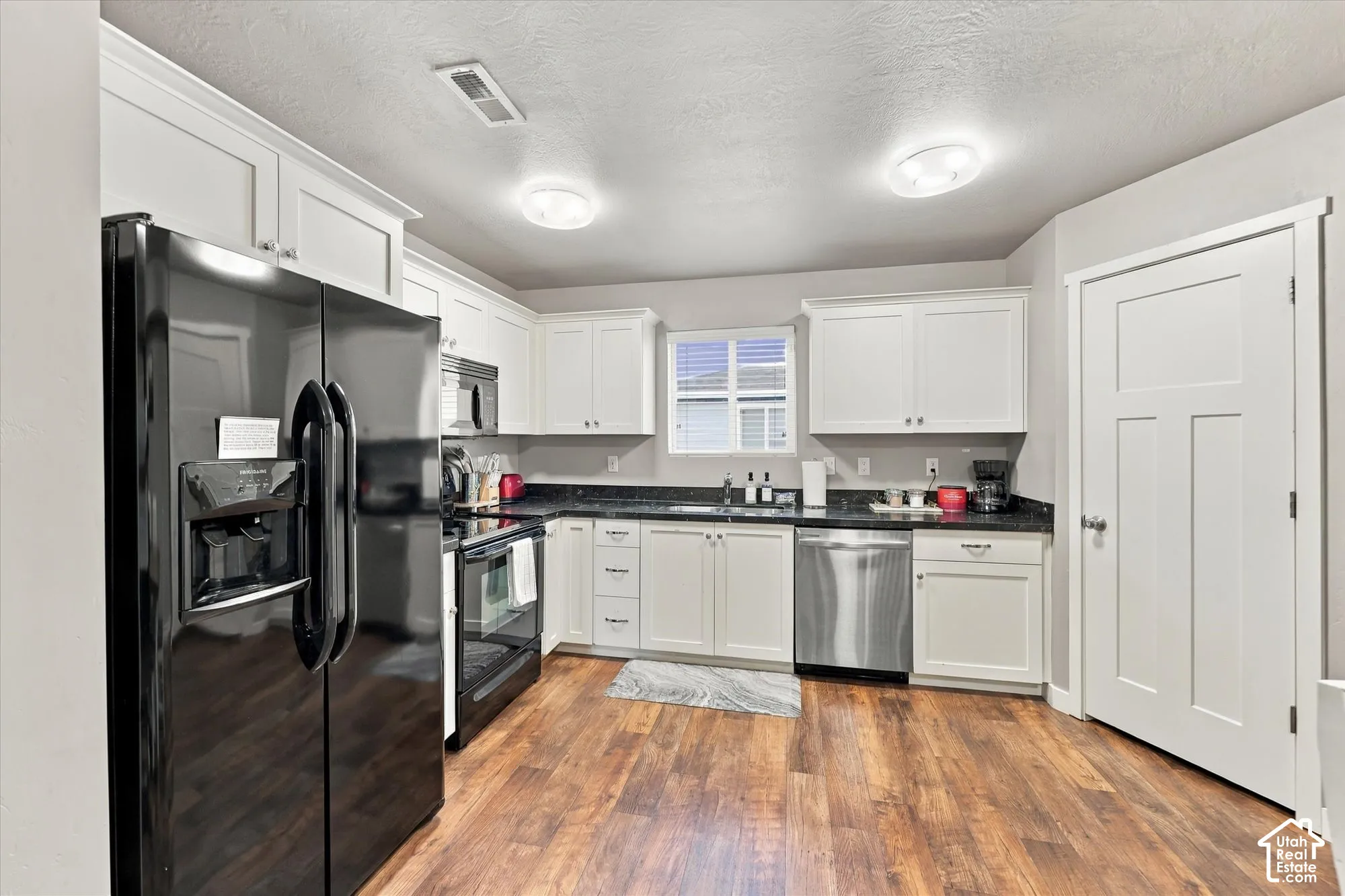 Kitchen featuring wood-finish flooring, white cabinetry, dark countertops, and stainless steel appliances
