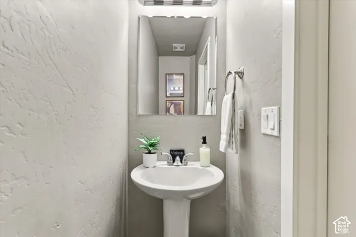 Pedestal sink with chrome faucet, framed mirror, and textured wall finish