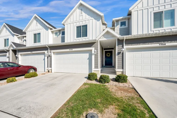 Modern townhome with board and batten siding, attached garage, concrete driveway, covered entry, and exterior lighting
