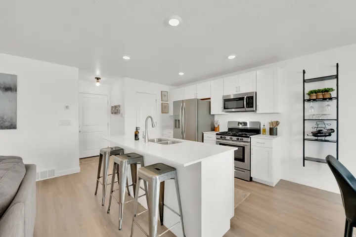 White cabinetry, stainless steel appliances, a kitchen island with seating, a stainless steel sink, and light wood-finish flooring