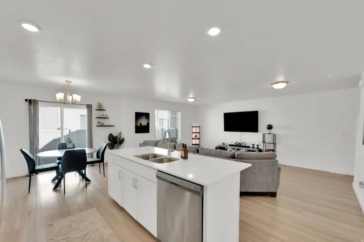 Open-concept living space featuring a kitchen island with dual sinks, light wood-finish flooring, recessed lighting, and a dining area with a chandelier