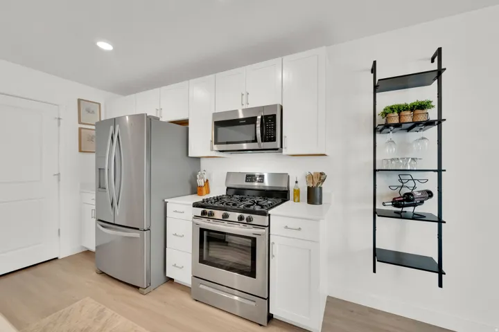 White cabinetry, stainless steel appliances, light wood-finish flooring, recessed lighting, and a wall-mounted shelving unit