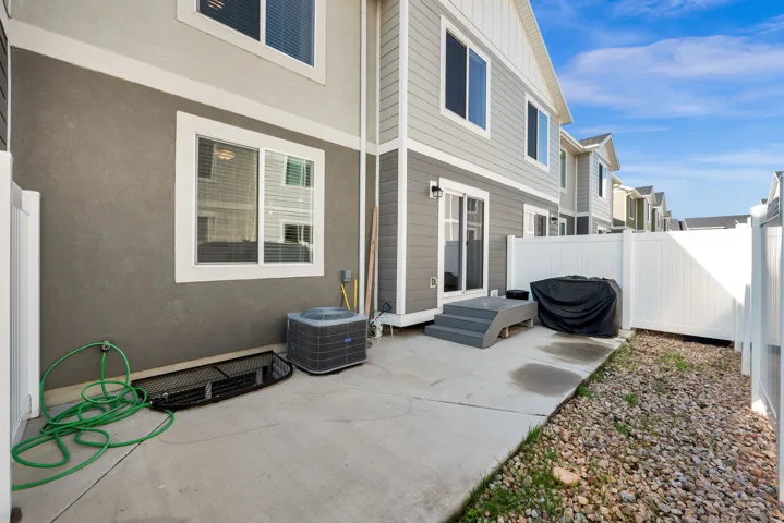 Concrete patio area featuring a white vinyl fence, exterior lighting, and a two-tone stucco and siding facade