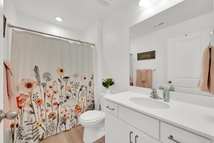 White vanity with integrated sink, chrome faucet, wall-mounted mirror, and recessed lighting