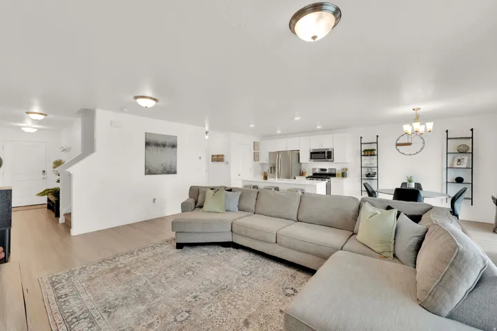 Open-concept living space featuring wood-finish flooring, recessed lighting, and a kitchen with white cabinetry and stainless steel appliances
