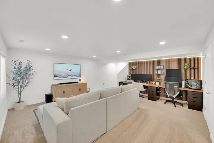 Recessed lighting throughout, wall-mounted television, wood-finish media console, built-in desk area with wood-finish top and dark cabinetry, and a slatted wood-finish accent wall with integrated lighting