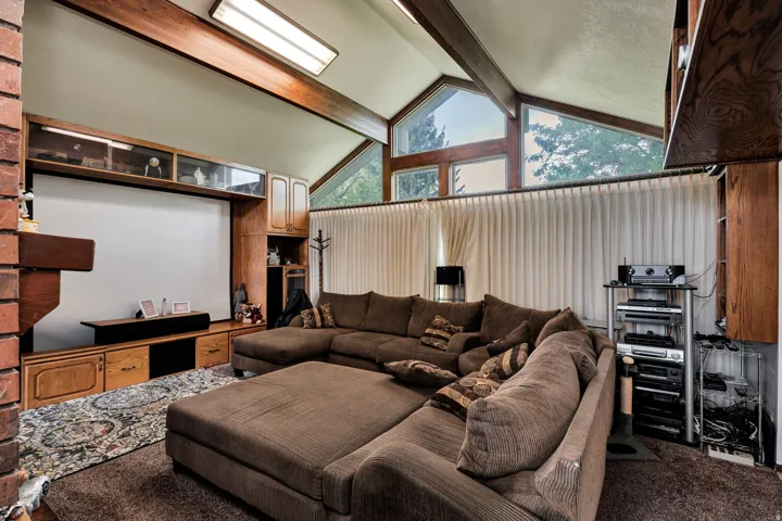 Vaulted ceiling with exposed wood beams, brick fireplace, built-in wood cabinetry, and triangular windows