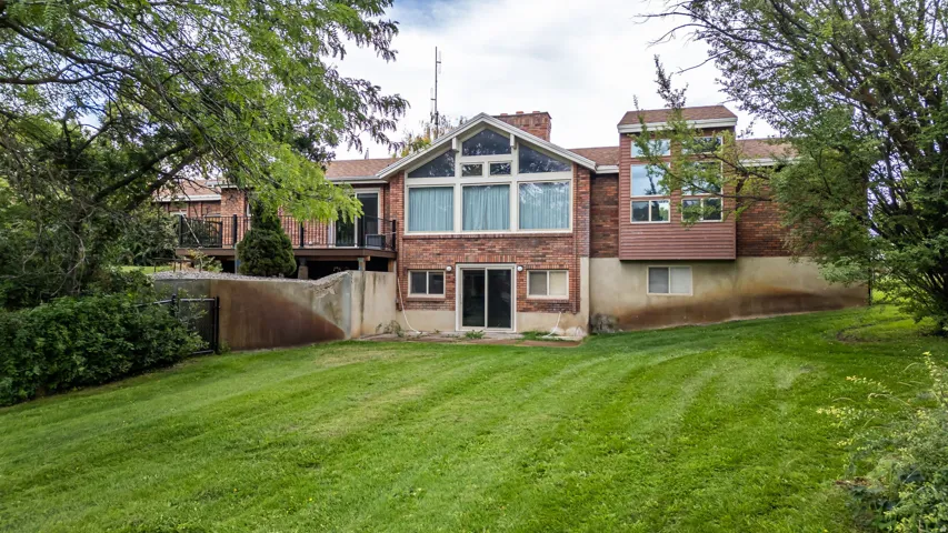 Brick exterior with a prominent A-frame window design, multiple upper-level balconies, and a ground-level sliding glass door opening to a sloped grassy yard