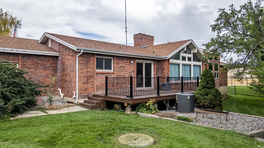 Brick exterior featuring a wood deck with black railings, a grass lawn, and a sloped gravel area