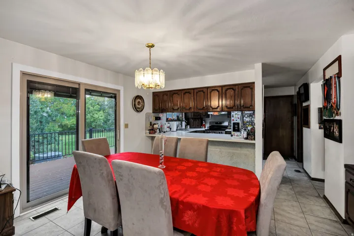 Sliding glass doors opening to an exterior deck with black railings, a kitchen pass-through, wood cabinetry, tile flooring, and a chandelier