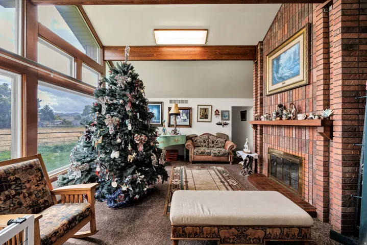 Brick fireplace with wood mantel, large picture windows, wood ceiling beams, and vaulted ceilings