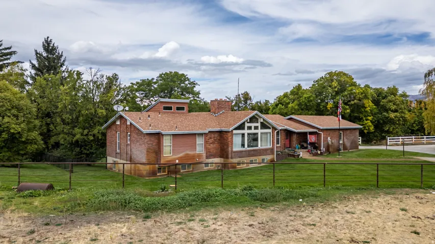 Brick exterior with multiple window styles, mature landscaping, and a fenced yard