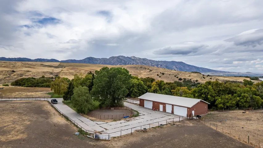 Expansive property featuring a multi-bay garage structure, substantial paved drive, mature trees, and mountainous terrain