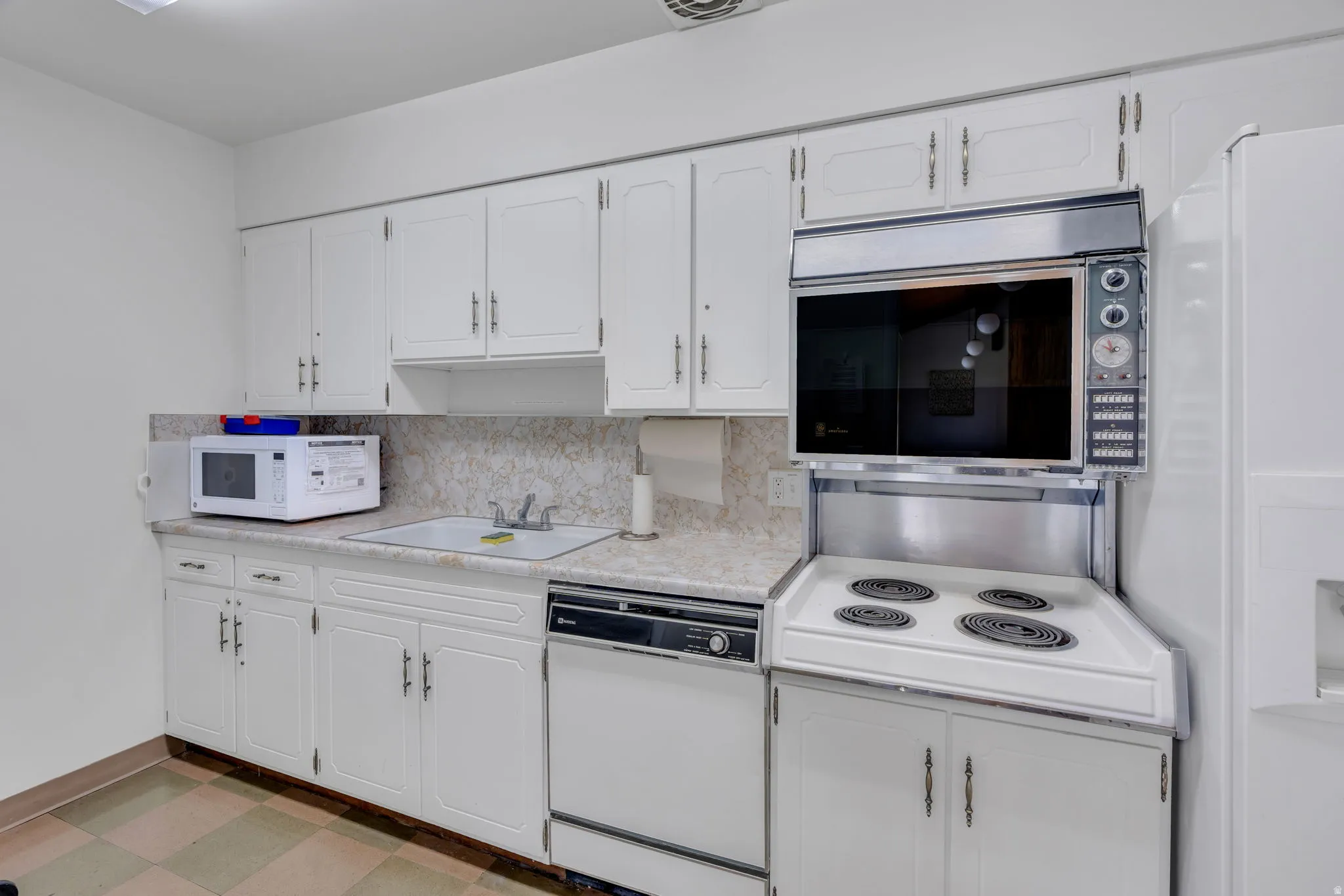 White cabinetry with silver-tone hardware, a drop-in sink, a built-in wall oven, a surface cooking range, and a dishwasher
