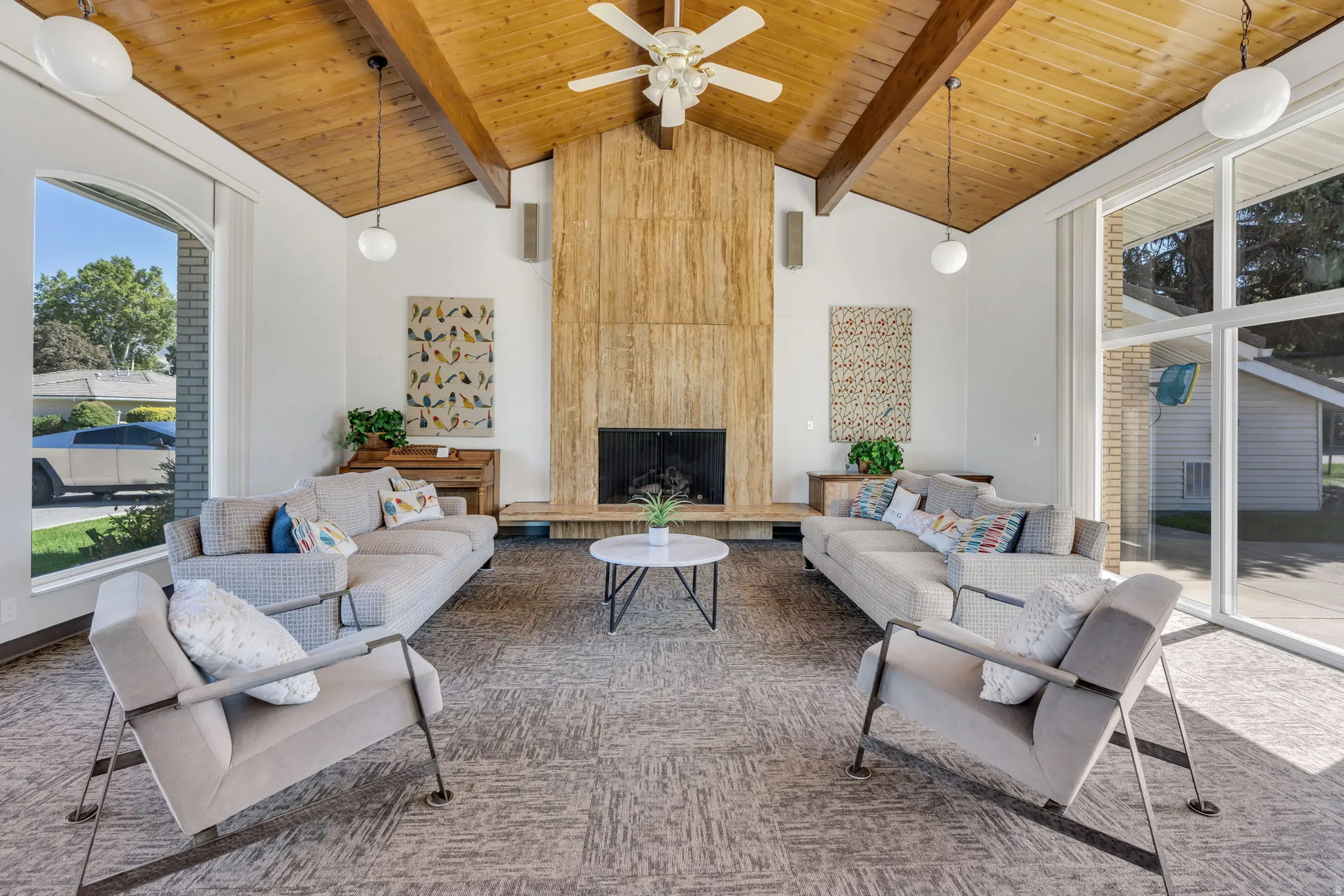 Vaulted wood-paneled ceiling with exposed beams, full-height stone fireplace, large arched window, and expansive sliding glass doors
