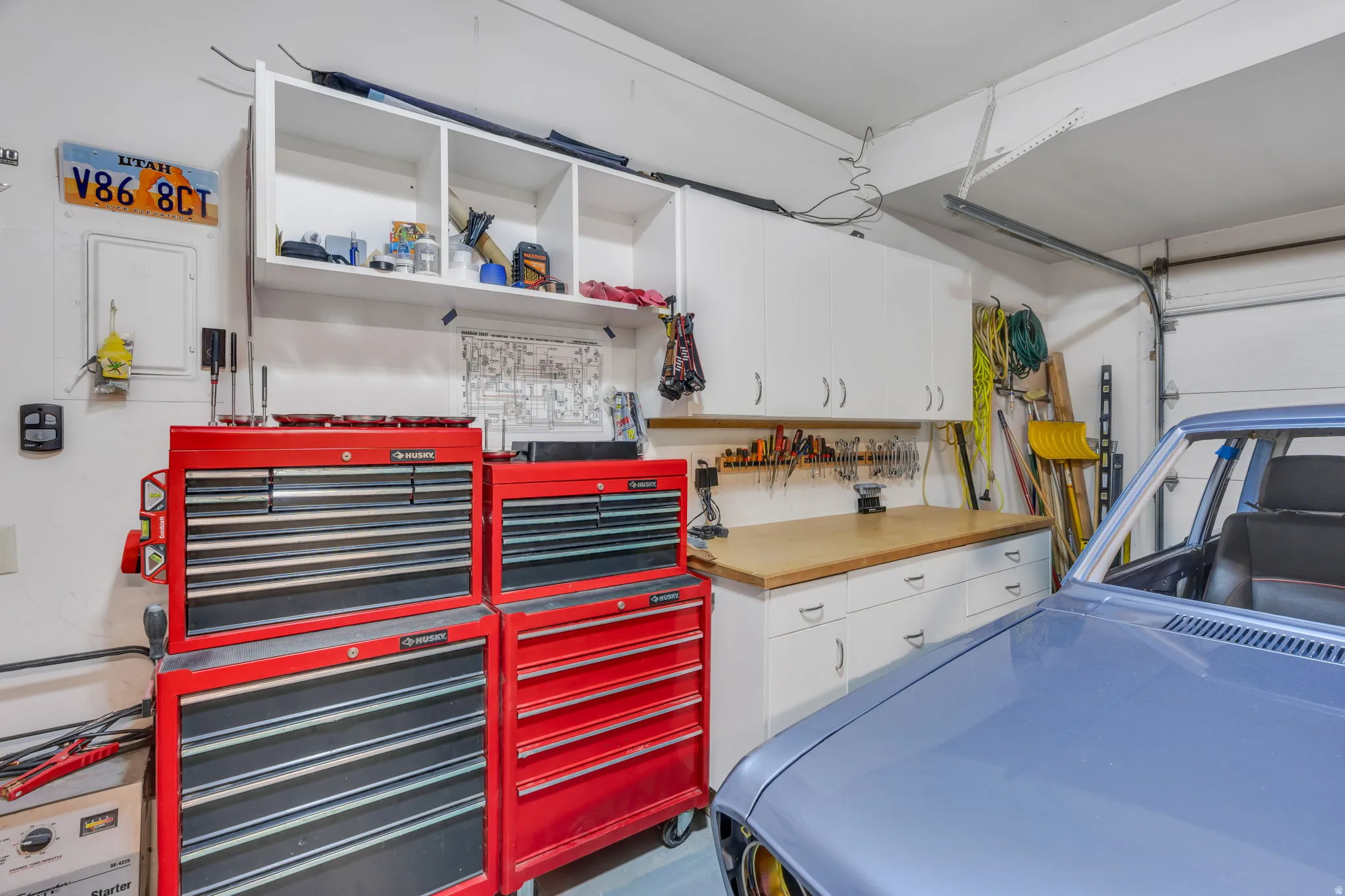White upper cabinetry, white base cabinetry, wood-finish countertop, white walls, and a visible garage door mechanism