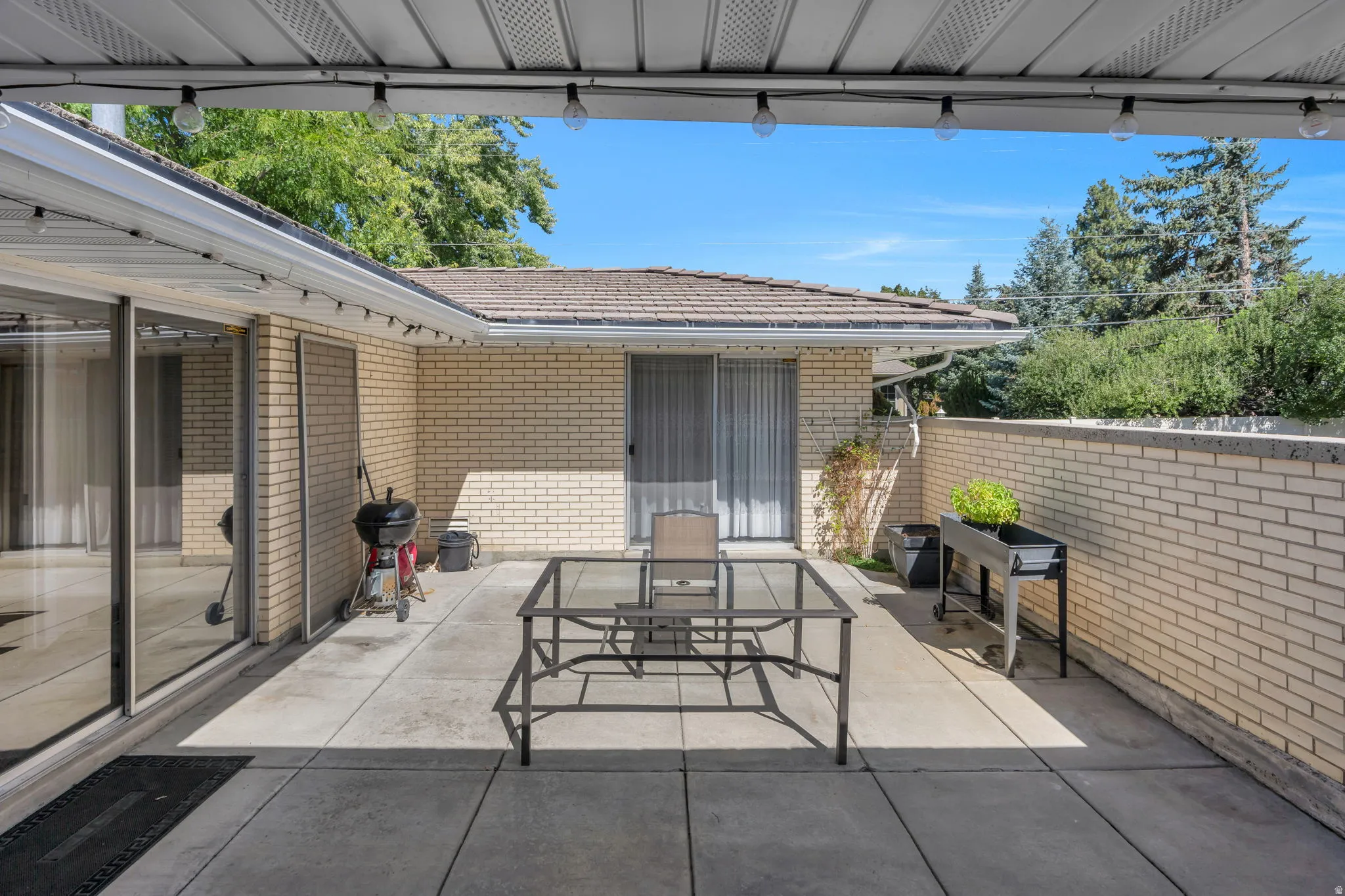 Covered concrete patio with overhead lighting, featuring a brick exterior and sliding glass door access