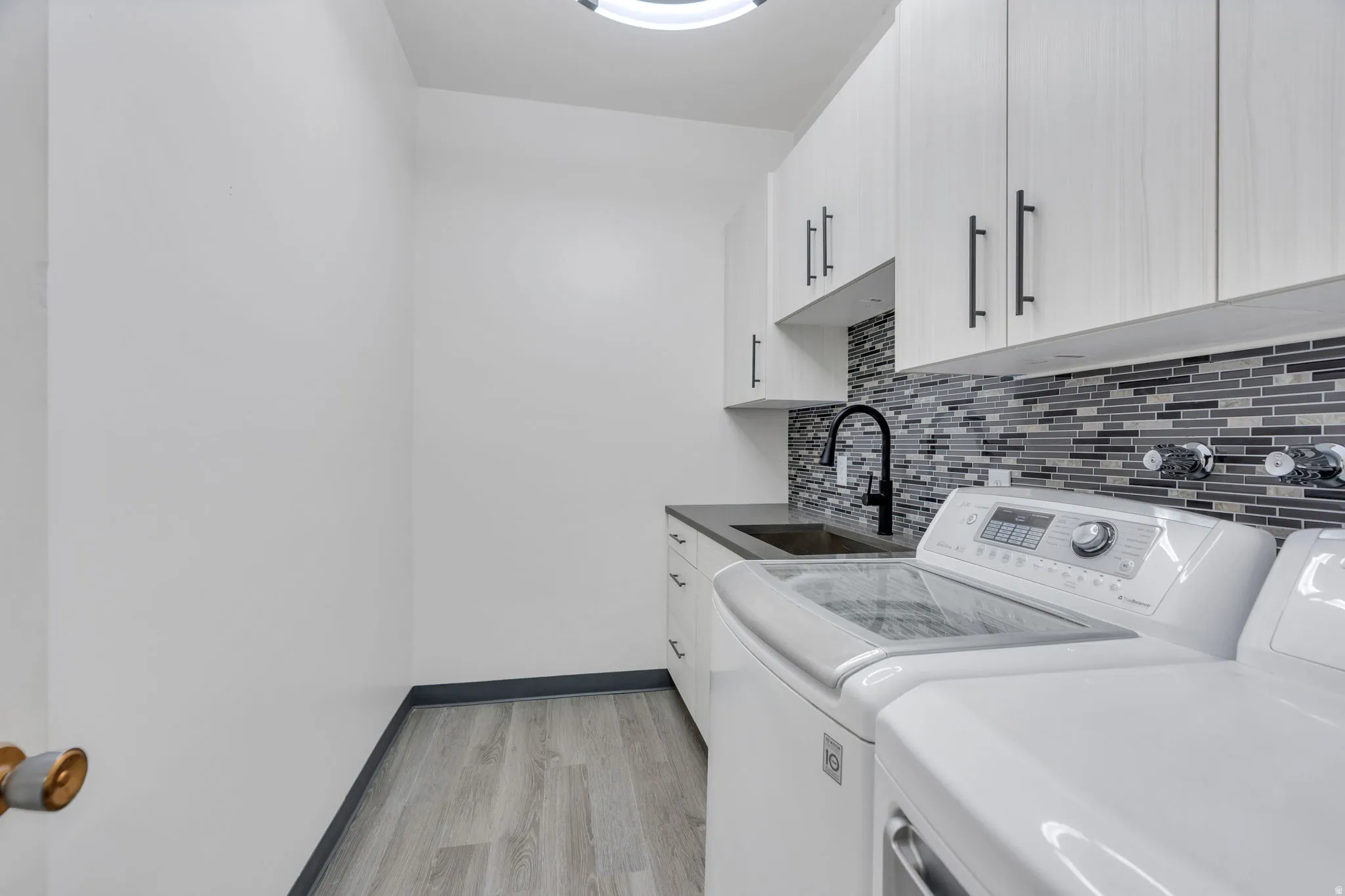 White cabinetry with dark pulls, dark countertop, and a mosaic tile backsplash